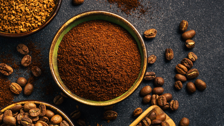 Coffee beans in a bowl with a wooden scoop of ground coffee