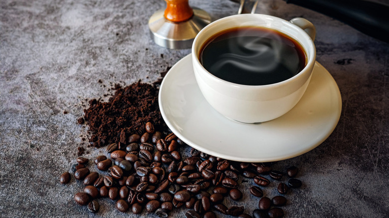 a cup of coffee next to whole beans and grounds
