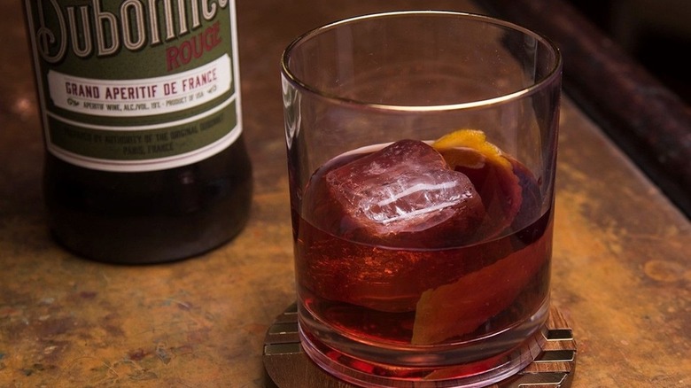 Dubonnet and gin cocktail with ice in a glass with a bottle of Dubonnet in the background