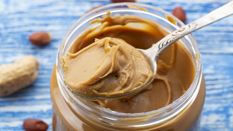 Spoon of peanut butter over open peanut butter jar