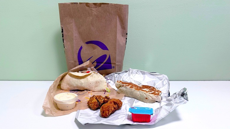 Taco Bell food items in front of a Taco Bell bag on a green and white background
