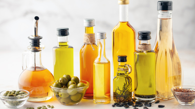 a variety of oils in pretty glass bottles with their whole ingredients in glass bowls