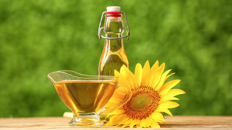 a bottle and glass bowl with sunflower oil next to a sunflower