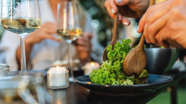 Person tossing green salad in a bowl