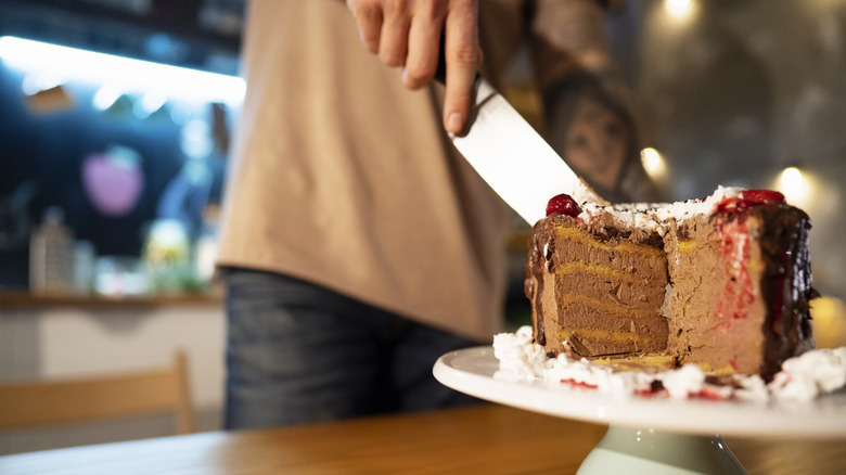 hand cutting chocolate cake in kitchen