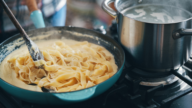 Fettuccine alfredo cooking in a blue pan with alfredo sauce