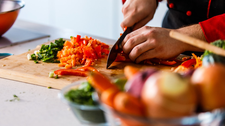 Chef prepping sofrito with green onion, carrot, and red pepper
