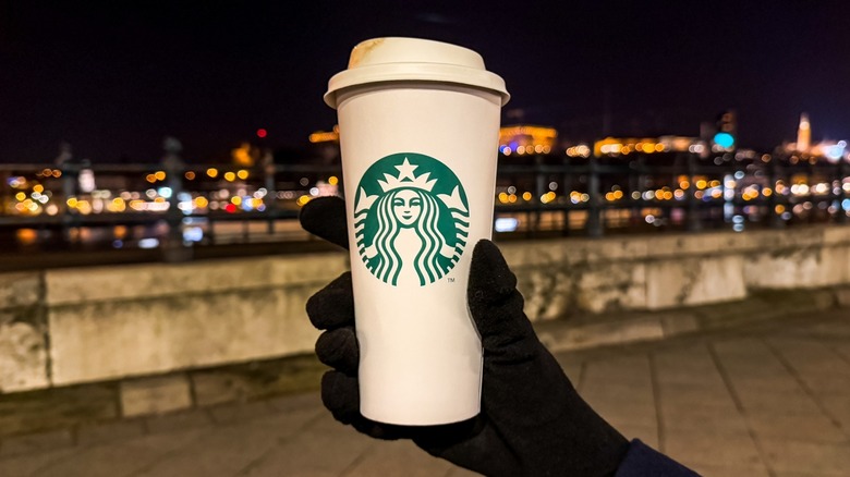 A gloved hand holding a hot Starbucks drink