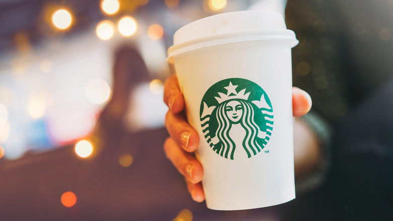 a person holding out a hot starbucks drink