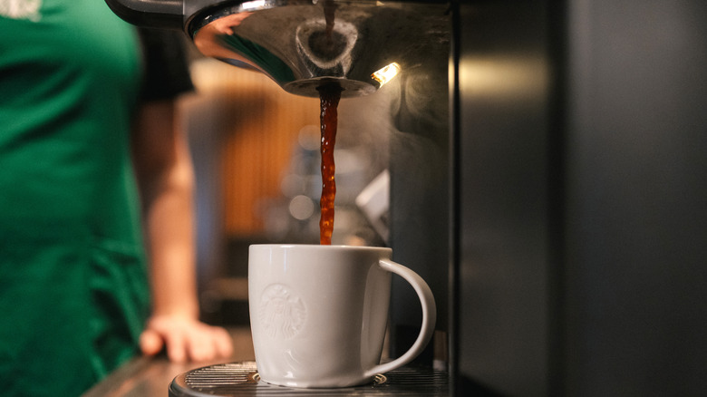 Starbucks coffee being brewed into white cup while barista in green smock is in background