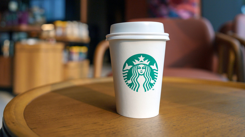 A white cup of Starbucks coffee sits on a brown table inside of a Starbucks