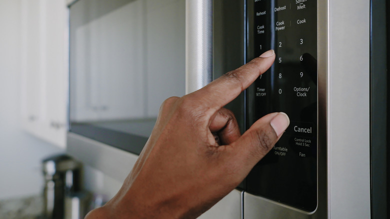 Person pressing buttons on a microwave oven