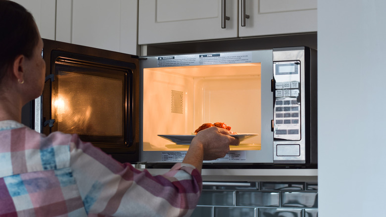 A woman putting a plate of food into the microwave