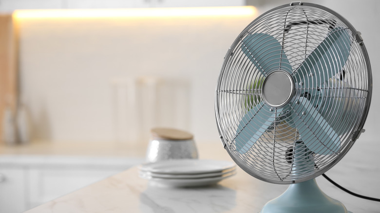 Electric fan on kitchen counter in front of plates