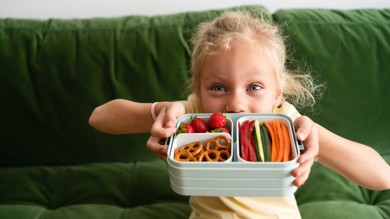A child holds a plastic box of healthy snacks.