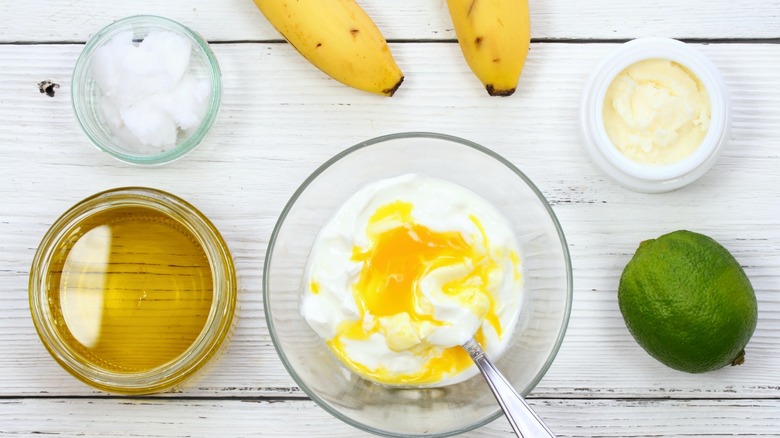 face mask ingredients such as honey, coconut oil, bananas, yogurt, and lime juice on white wood