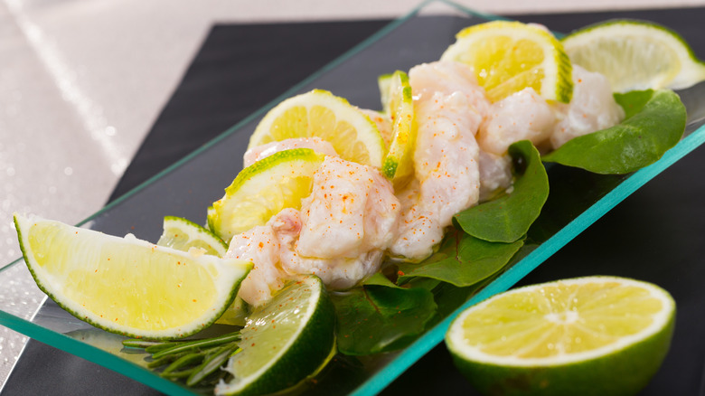 lime slices on glass platter with raw, seasoned fish pieces