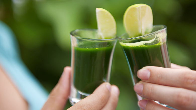 two shots of green juice with lime slices in two hands
