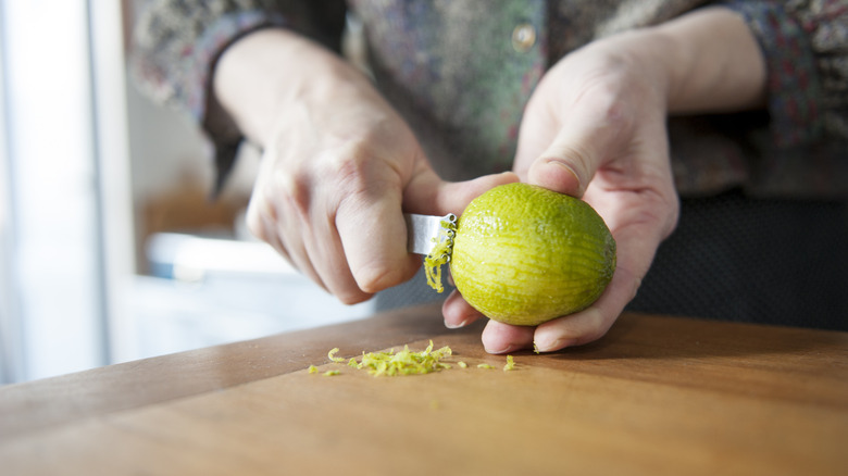 woman zesting a lime on wooden surface