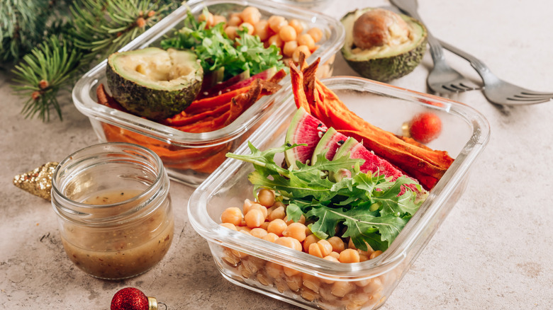 two glass containers with meal-prepped foods by salad dressing