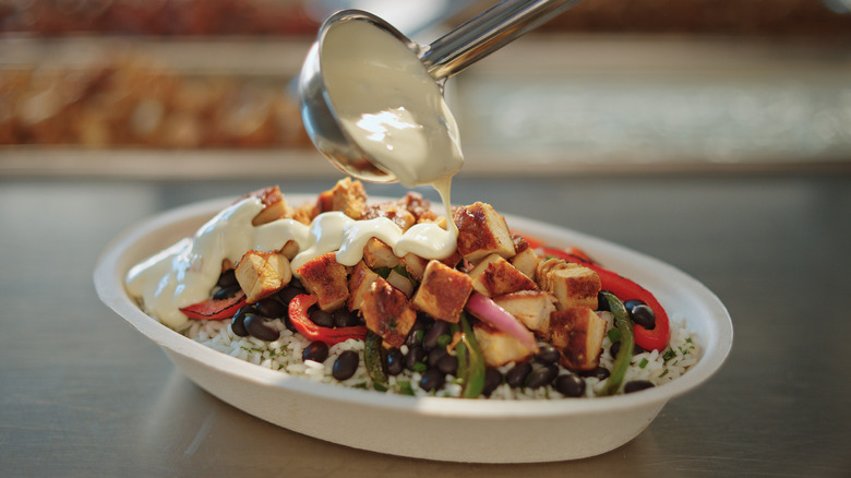 Spooning queso topping over burrito bowl