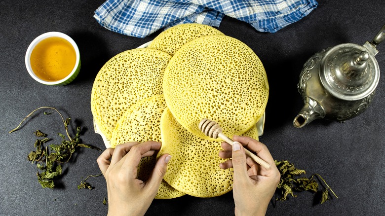 Hand spreading honey onto baghrir