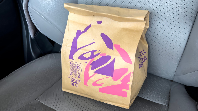 A brown bag of Taco Bell takeout in a car seat