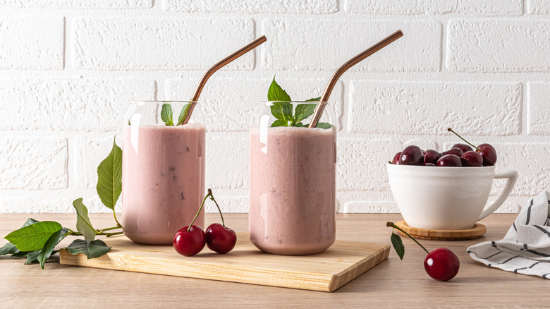 Cherry smoothies with herbs and metal straws and more herbs and cherries on the counter and in a tea cup