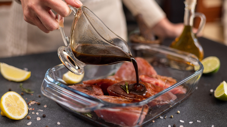 Hand pouring marinade over meat