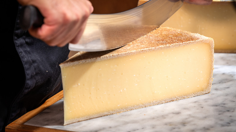 A man slices a block of gruyere with a cheese knife