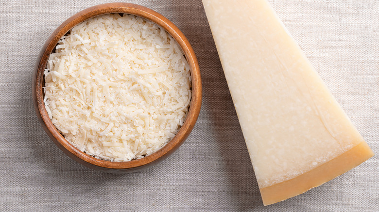 A block of parmesan cheese, with a bowl of grated parmesan next to it