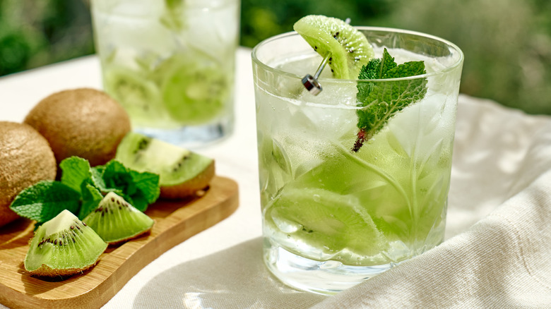 Kiwi drinks garnished with mint leaves, alongside sliced and whole kiwis