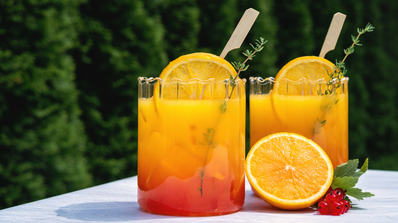 Two tequila mixed drinks with orange slices and thyme sprigs