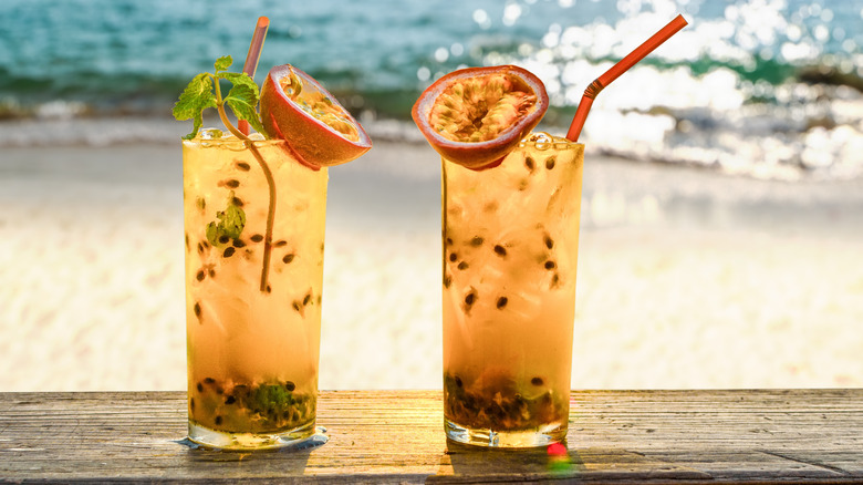 Two passionfruit cocktails on a table with a beach in the background