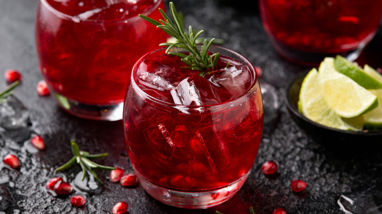 Multiple pomegranate cocktails with seeds and lime wedges with garnished with rosemary sprigs