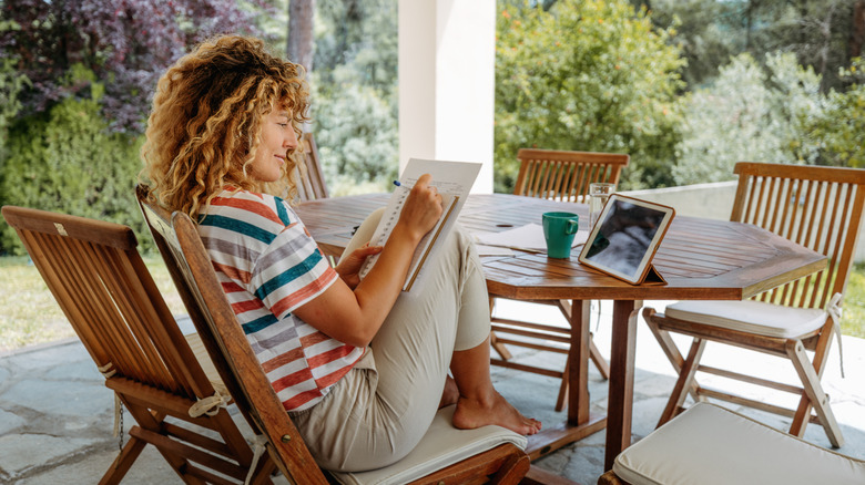 A woman makes notes on a notepad while sitting in her backyard