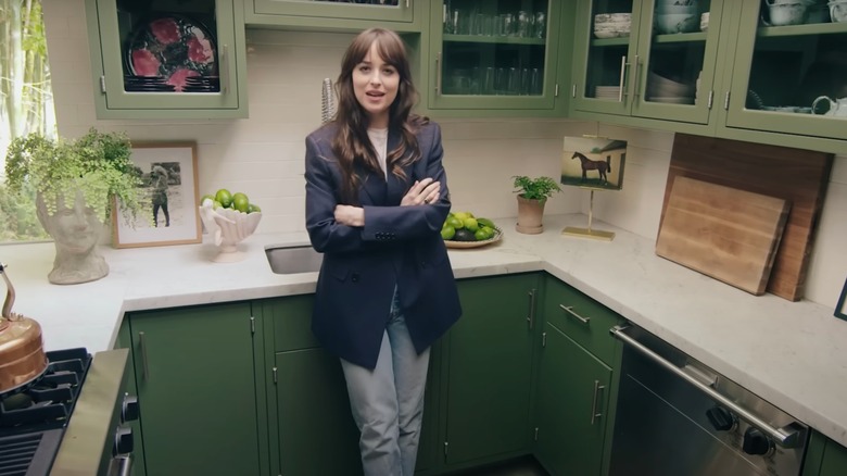 Dakota Johnson stands in her kitchen, with clear glass-paneled cabinets behind her