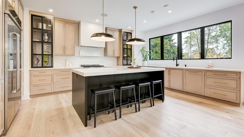 The interior of a modern kitchen, featuring a black and white island and wooden cupboards