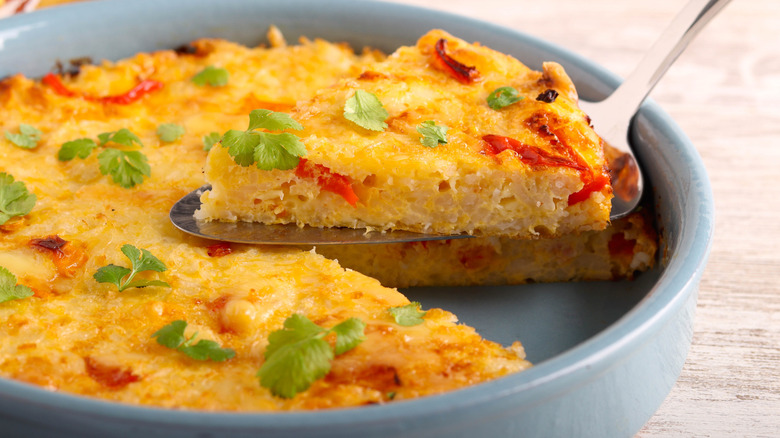 Rice frittata made with green herbs and red pepper slices, with one slice held up on a spatula