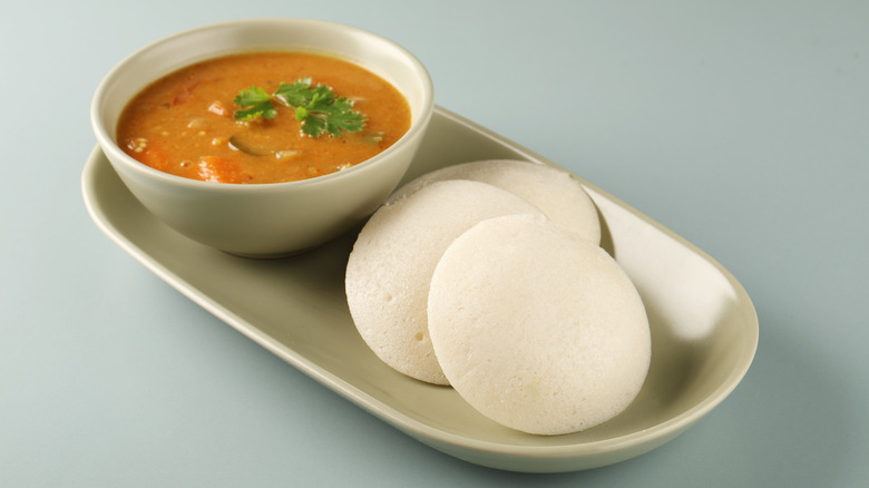 Idli on a plate with a bowl of sambar
