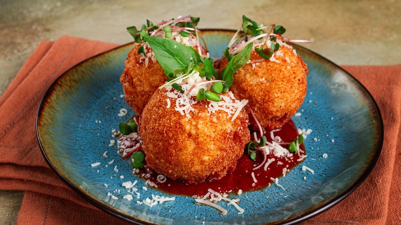 A plate of arancini, with sauce, topped with fresh herbs and Parmesan cheese