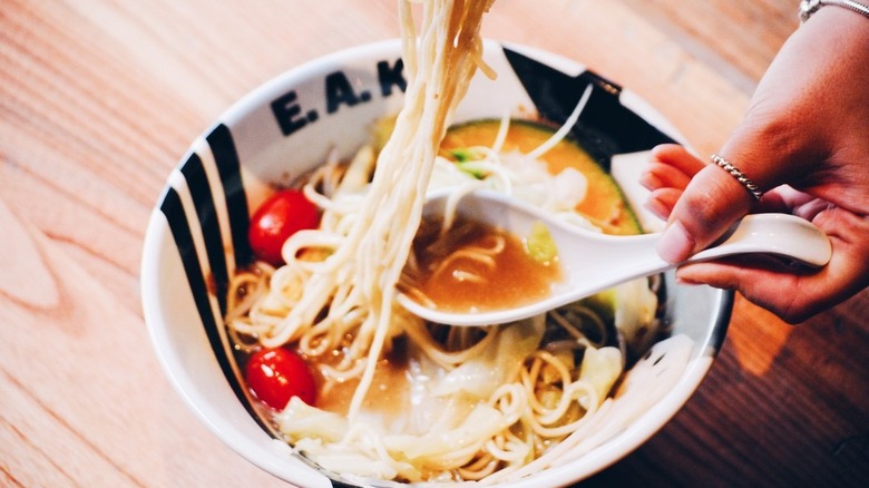 Spoon in ramen noodle broth with tomatoes