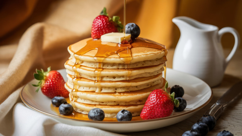 Close-up of pancakes on yellow plate with fruit on top and syrup dripping over the sides