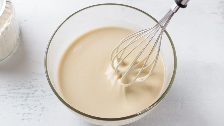 Whisk standing up in a glass bowl of pancake batter on a white countertop