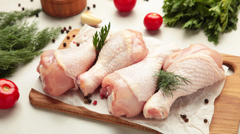 Raw chicken drumsticks with spices on cutting board
