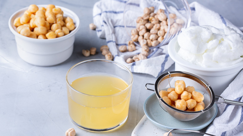 aquafaba in a glass bowl with chickpeas in a strainer and whipped aqua faba