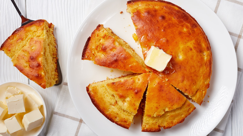 Homemade cornbread slices and butter on a kitchen table.