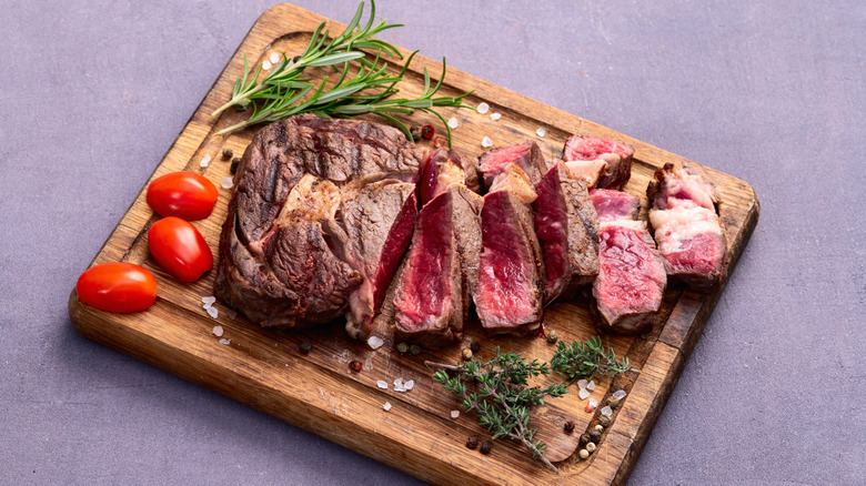 Very rare steak sliced on wooden cutting board with herbs and cherry tomatoes