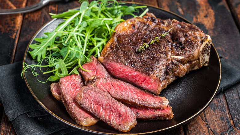Sliced rare steak on black plate with greens