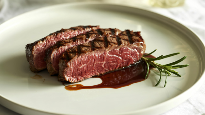 Sliced, medium-rare steak on white plate with garnish